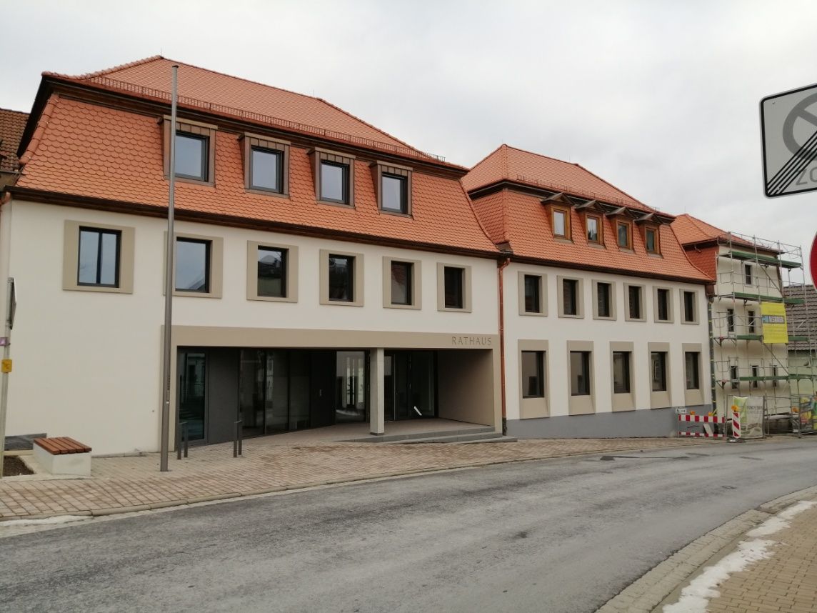 Gebäude mit rotem Ziegeldach und cremefarbener Fassade an einer Straße mit bewölktem Himmel.