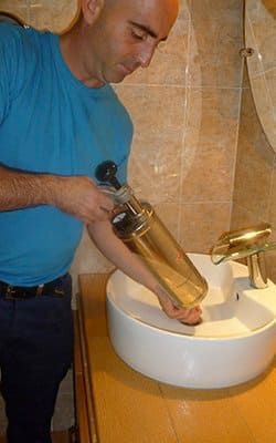 Un hombre está limpiando un lavabo del baño con una aspiradora.