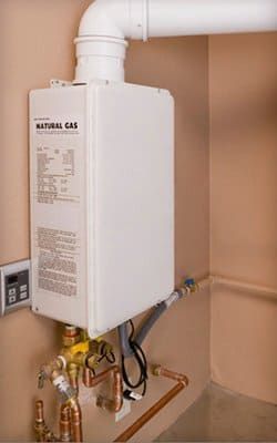 Un calentador de agua blanco está sentado en un rincón de una habitación al lado de tuberías de cobre.