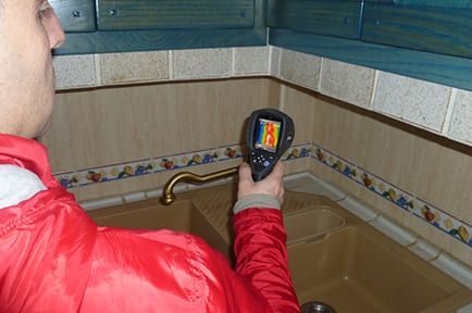 Un hombre con una chaqueta roja sostiene un termómetro sobre un fregadero.