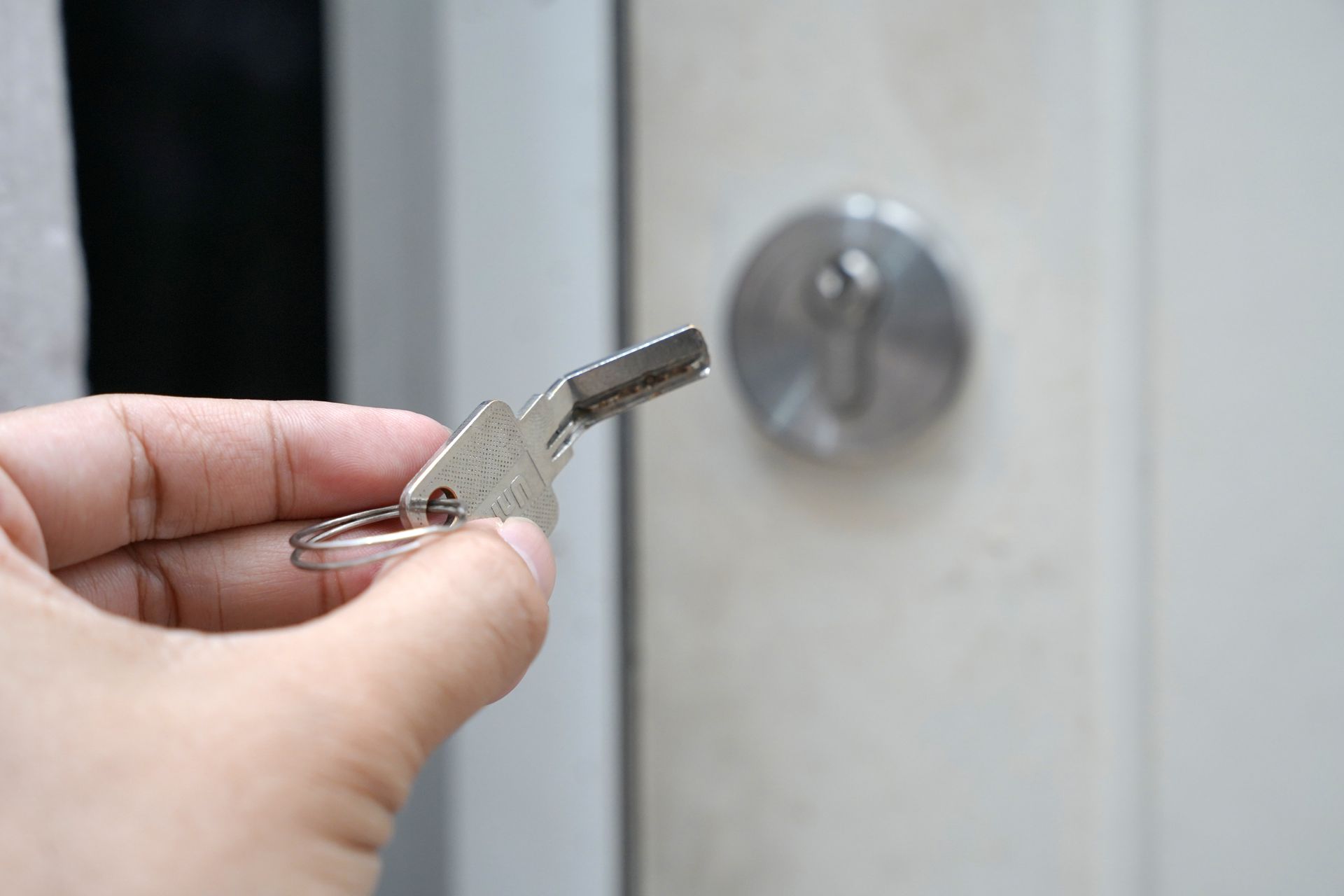 Une main tient une clé métallique vers la serrure d'une porte blanche.