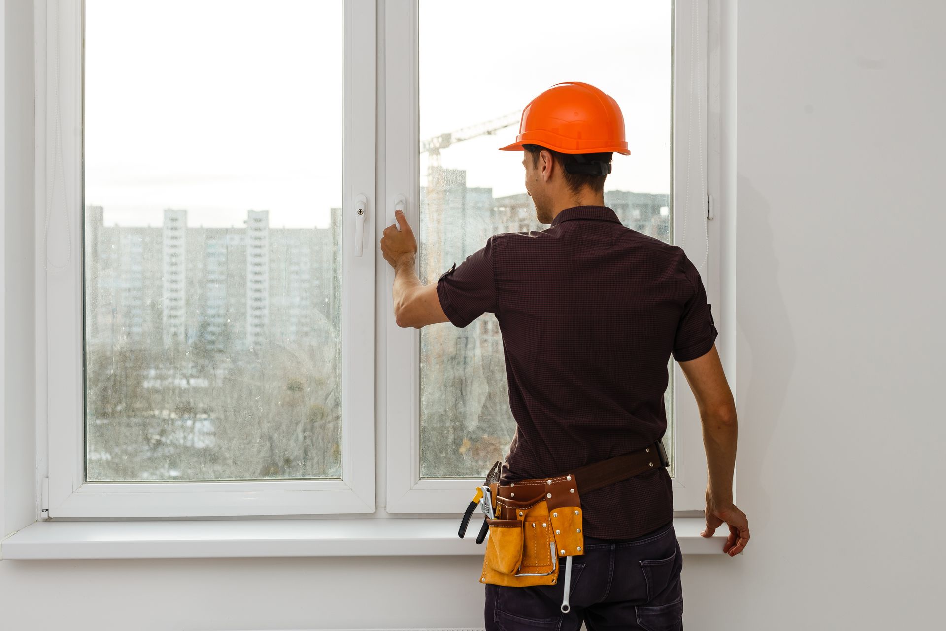Un ouvrier du bâtiment se tient à l'intérieur et ajuste un cadre de fenêtre blanc.