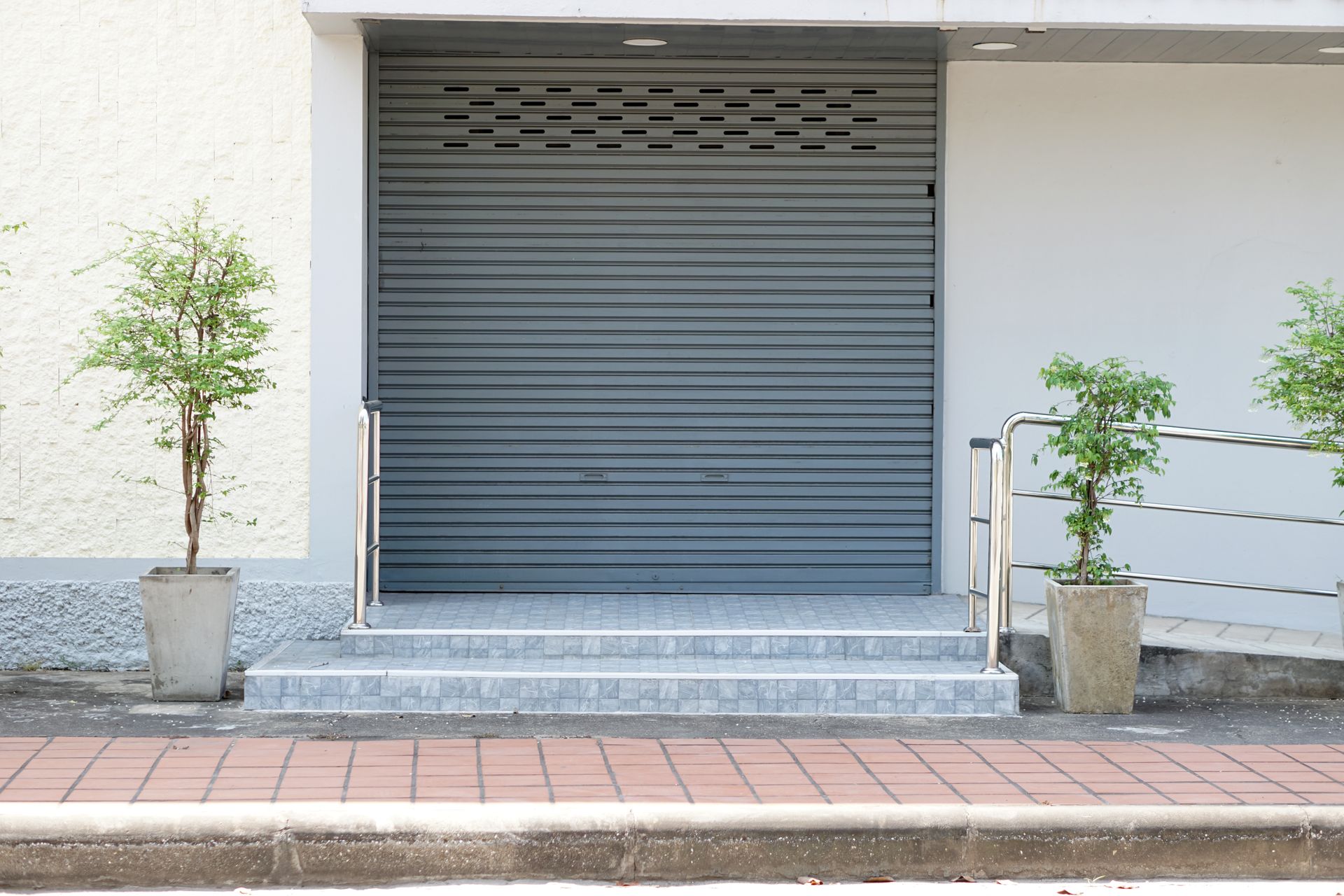 Porte de sécurité coulissante grise fermée à l'entrée d'un immeuble avec marches.