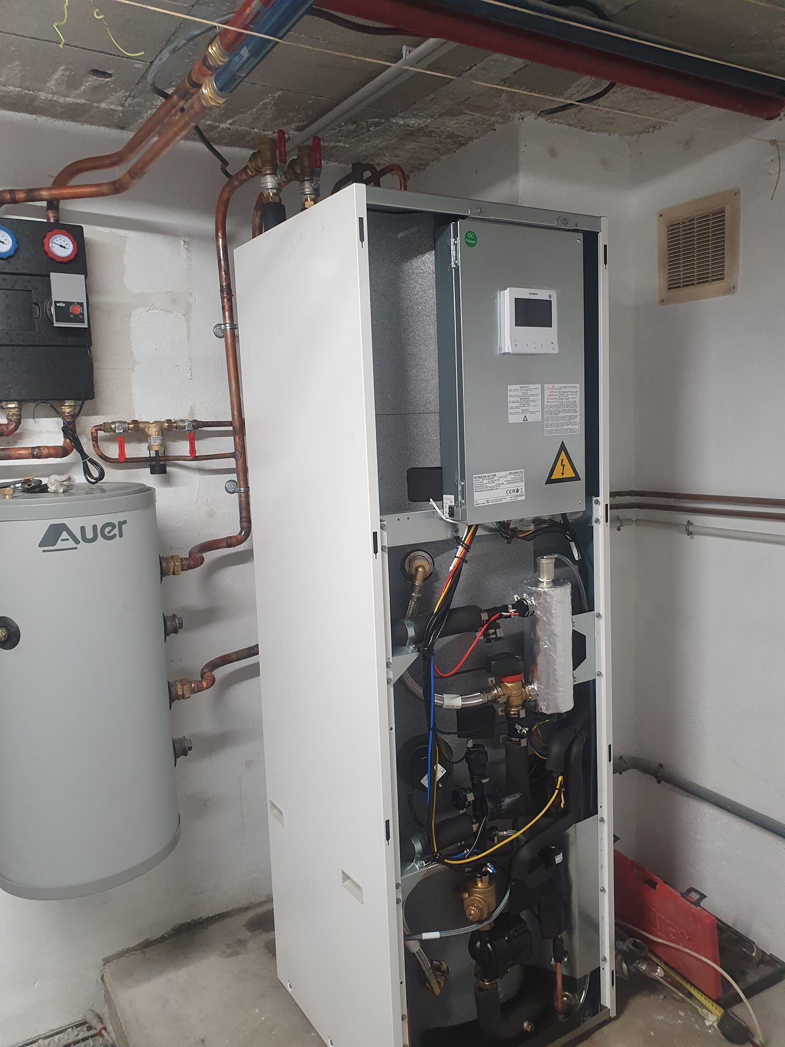 Une pompe à chaleur dont les panneaux ont été retirés, révélant les composants internes et la tuyauterie dans un local technique.