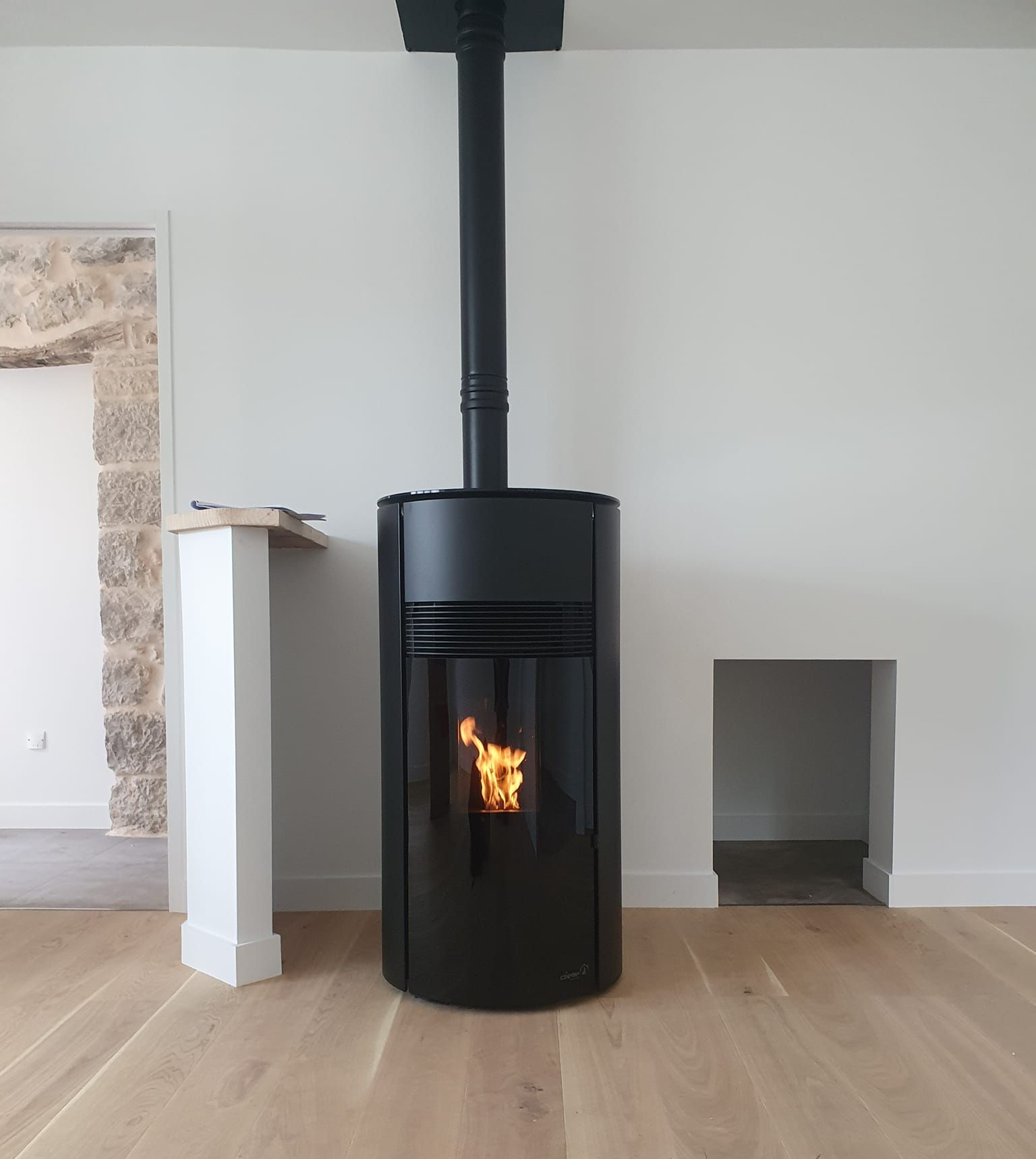 Poêle à granulés noirs avec des flammes, placé au centre devant un mur blanc et un parquet clair.