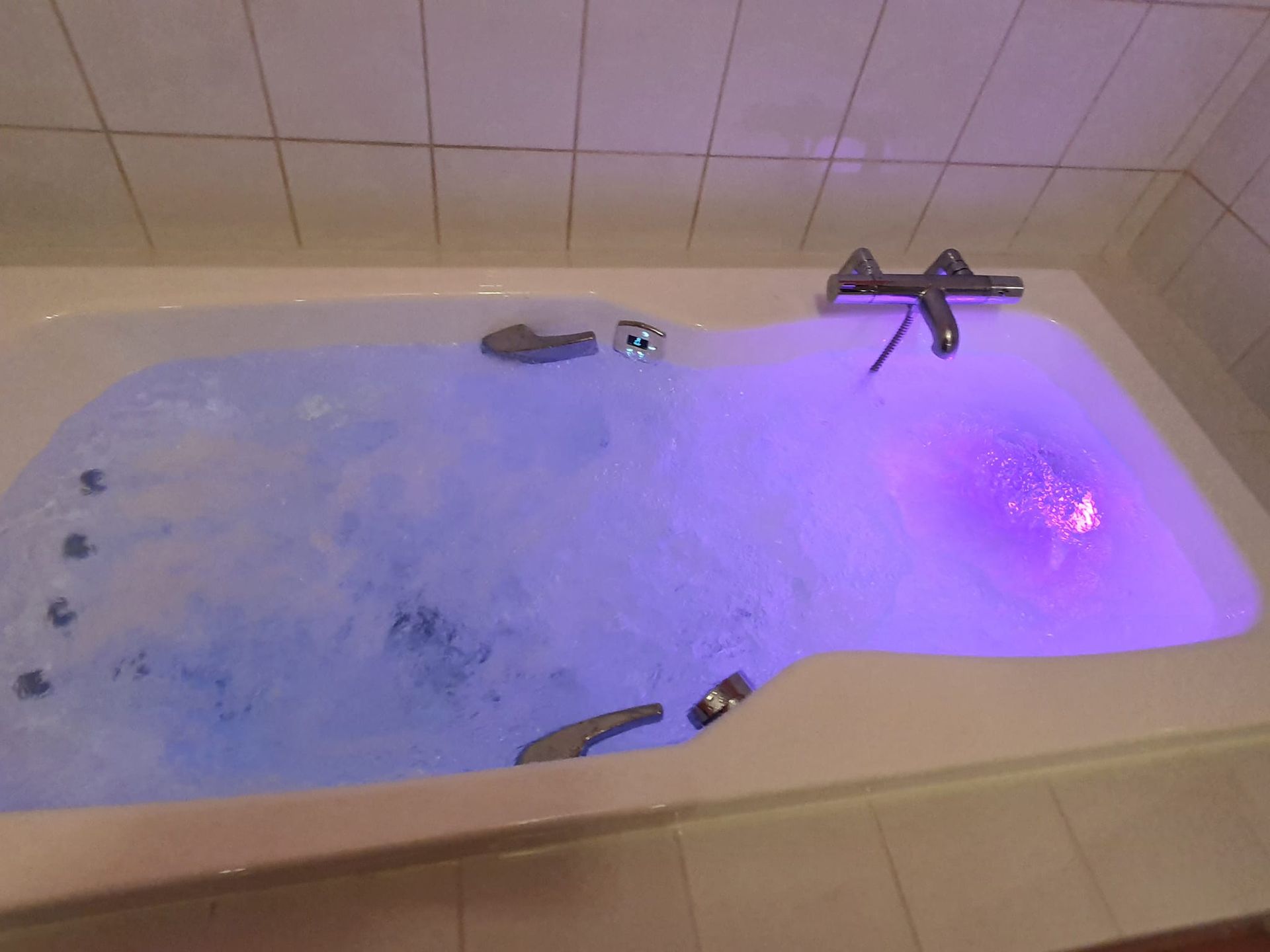 Un jacuzzi éclairé, rempli d'eau bouillonnante et illuminé par des lumières bleues et violettes.