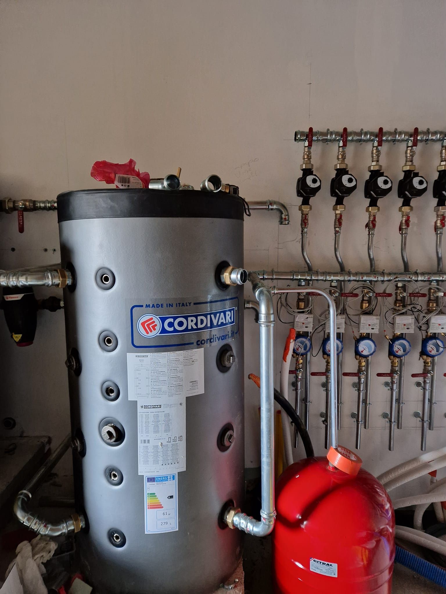 Un chauffe-eau et un vase d'expansion rouge reliés par des tuyaux, fixés au mur.