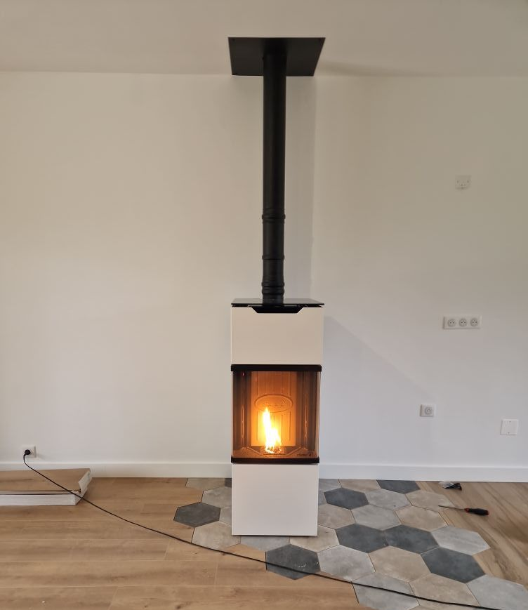 Poêle à granulés blanc et noir avec flamme, cheminée noire. Installé dans une pièce avec parquet et carrelage hexagonal.