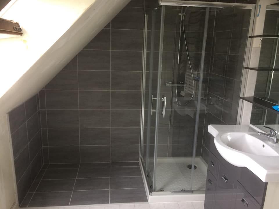 Salle de bains avec murs carrelés gris, douche et lavabo sous un plafond en pente.