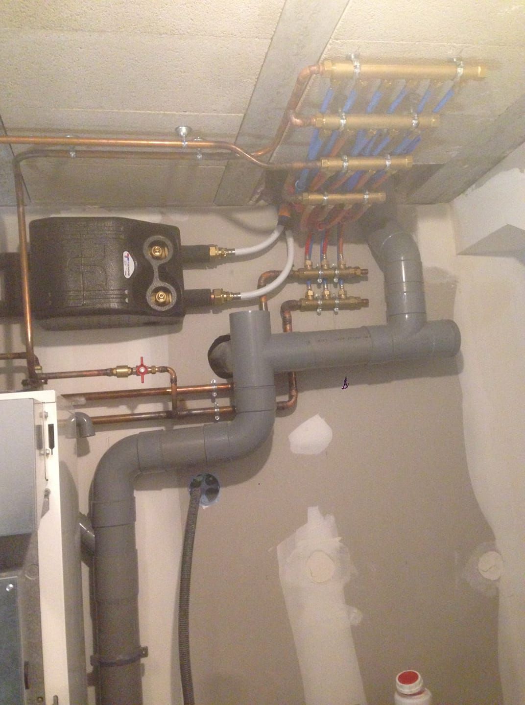 Tuyaux de plomberie de tailles et de matériaux variés sur un mur et un plafond de sous-sol.