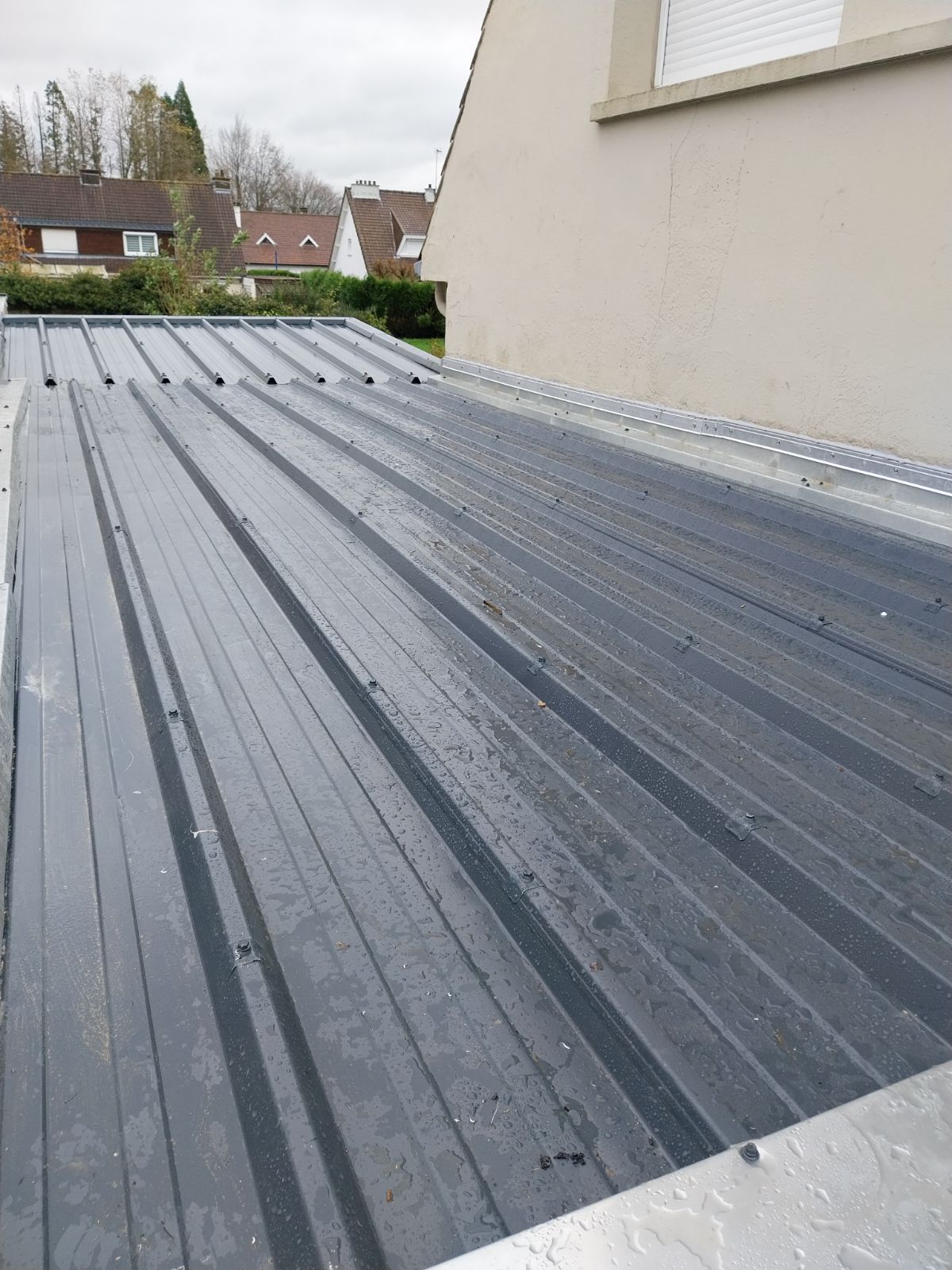 Toit en tôle ondulée grise sur l'extérieur d'un bâtiment, journée nuageuse.