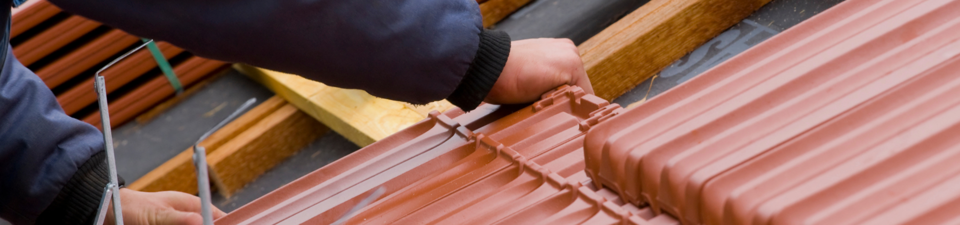Pose de tuiles brun rougeâtre. Mains sur les tuiles, travail avec des outils sur un toit.