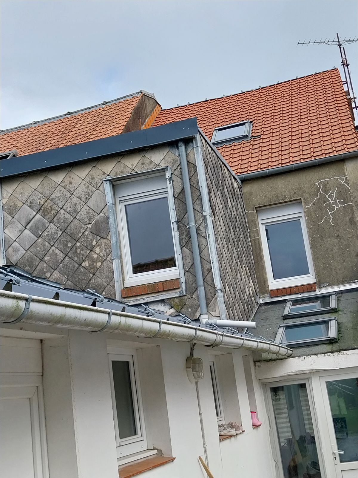 Vue extérieure d'un bâtiment avec un toit en ardoise et des lucarnes, sur fond de ciel nuageux.
