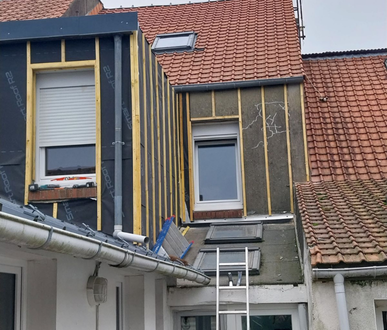 Extérieur d'un bâtiment en construction, avec montants apparents, isolation et installation de fenêtres.