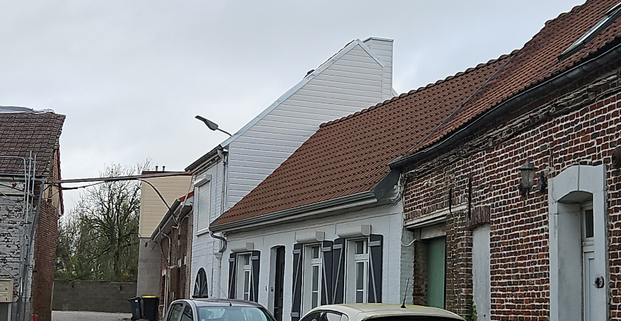 Rangée de bâtiments en briques et blancs avec des toits de tuiles orange sous un ciel nuageux.