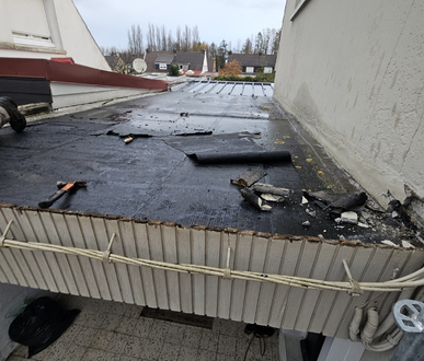 Toiture plate en réparation, avec papier goudronné retiré et outils. Vue extérieure.
