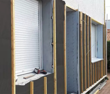 Extérieur maison en construction, ossature bois autour des fenêtres, isolation grise.