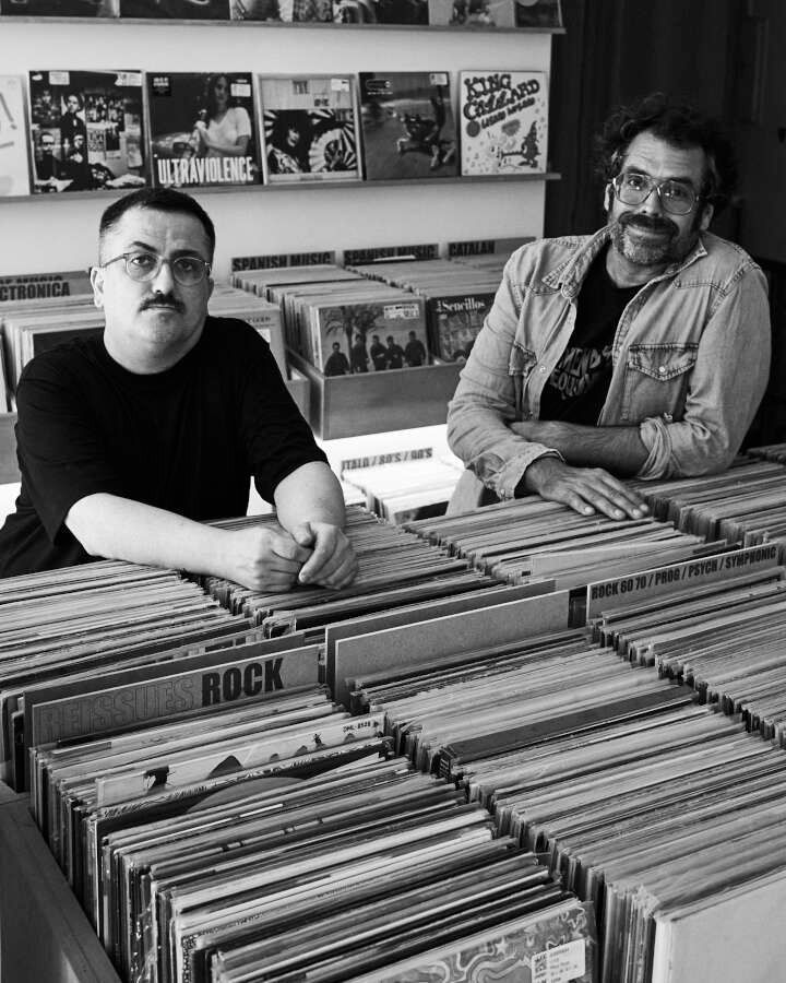Dos hombres están sentados en una mesa llena de discos.