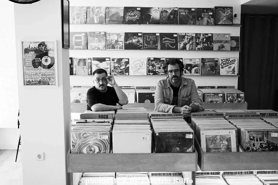 Dos hombres están sentados en un mostrador en una tienda de discos.
