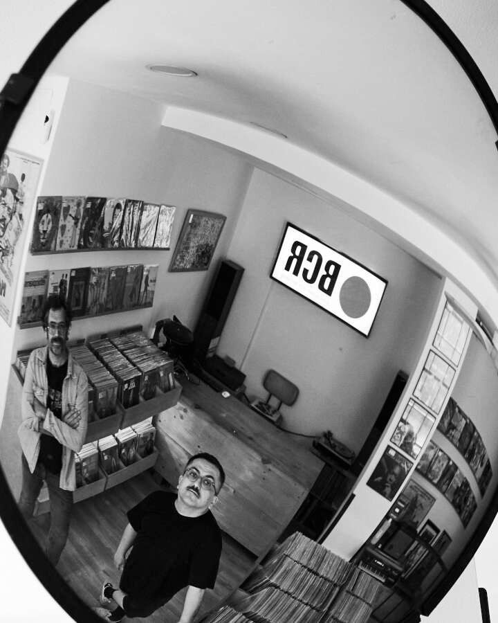 Una fotografía en blanco y negro de dos hombres en una habitación con un cartel en la pared que dice BBC.