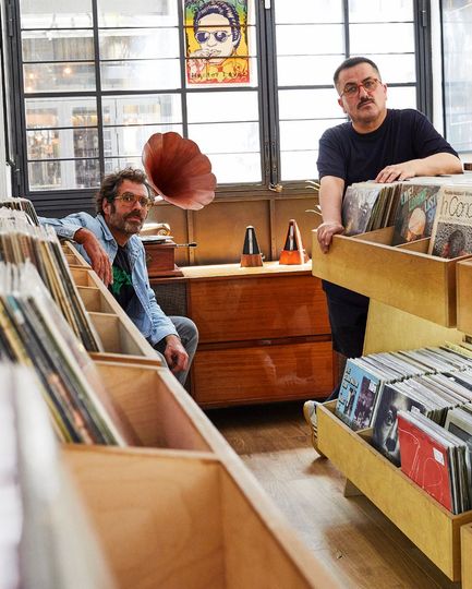 Dos hombres están parados frente a un tocadiscos en una tienda de discos.