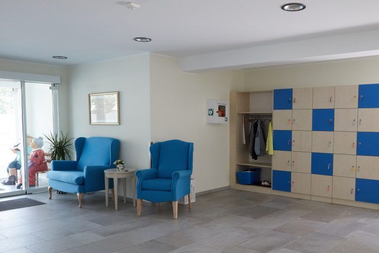 Helle Lobby mit blauen Stühlen, kleinem Tisch, Schließfächern und einem Eingang aus Glas