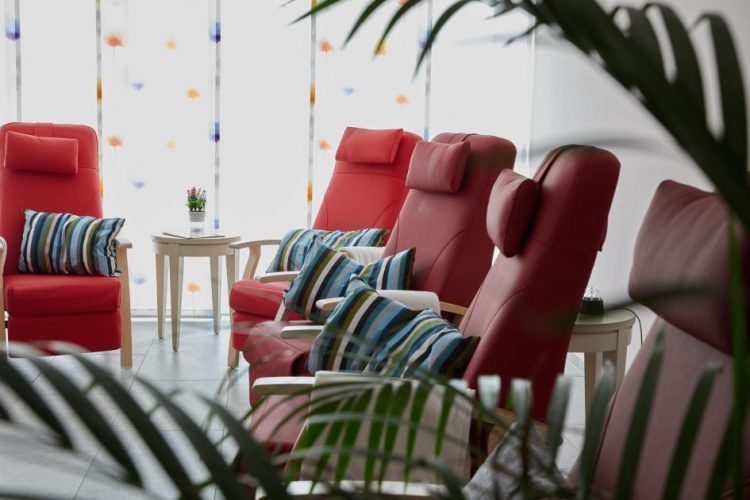 Rote Sessel mit gemusterten Kissen in einer hellen Lounge, umrahmt von grünen Pflanzen und einem kleinen Tisch.