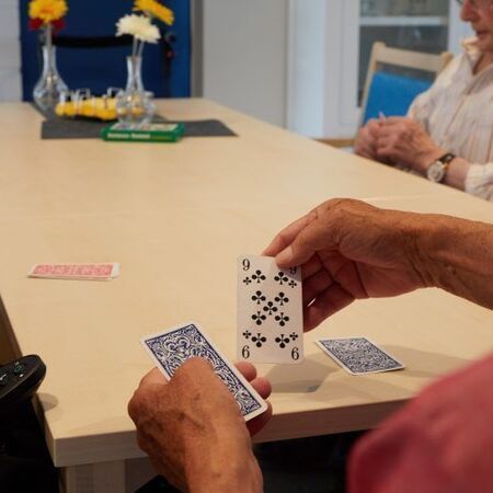 Hände, die während eines Kartenspiels Spielkarten an einem Tisch halten, wobei eine Karte verdeckt und eine Karte offen liegt.