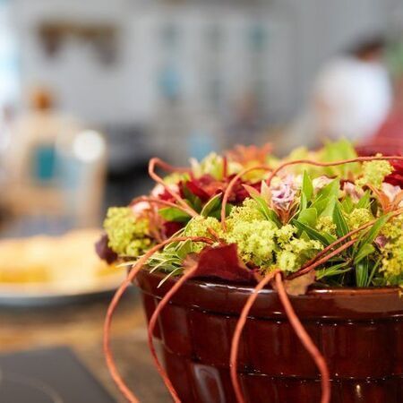 Eine Schüssel mit frischem Salat und roten Blättern in einer rustikalen Holzschüssel steht auf einem Tisch, im Hintergrund ist ein Essbereich zu sehen.