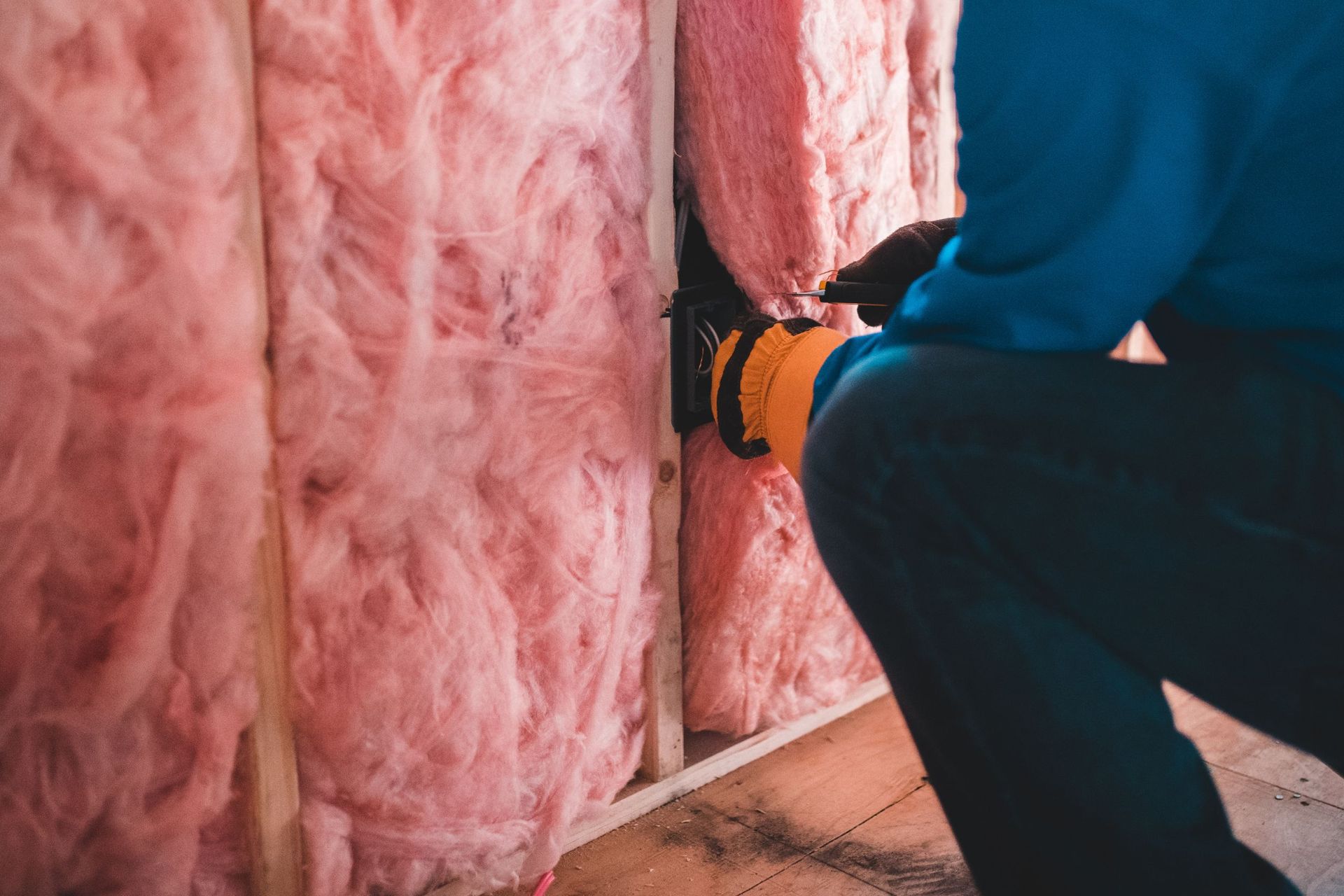 Un hombre está instalando un aislamiento rosa en una pared.