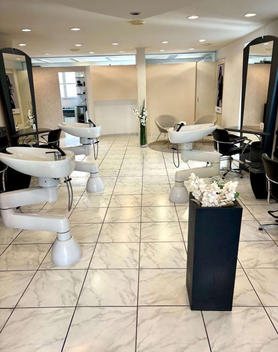 Heller Saloninnenraum mit weissen Waschbecken und Friseurstühlen auf Fliesenboden