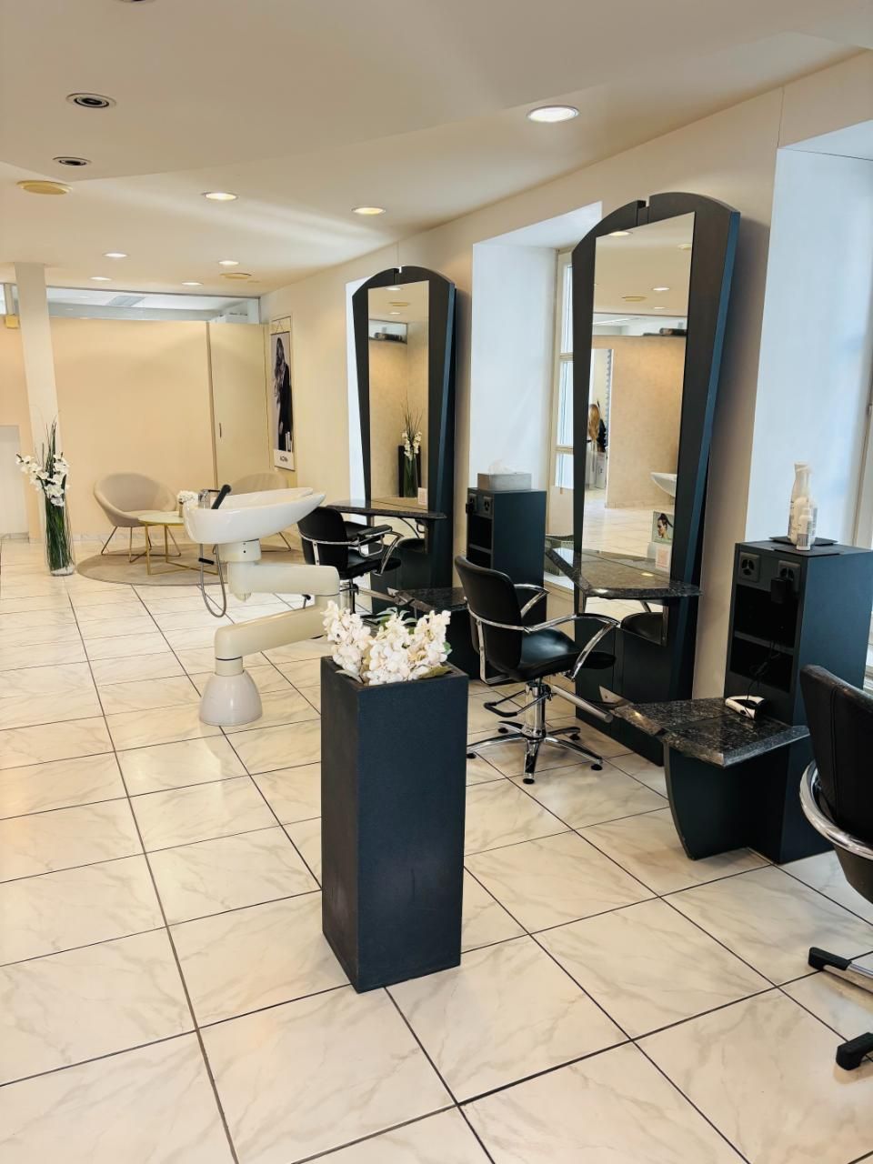 Heller Saloninnenraum mit Friseurstühlen, Spiegeln und Fliesenboden.