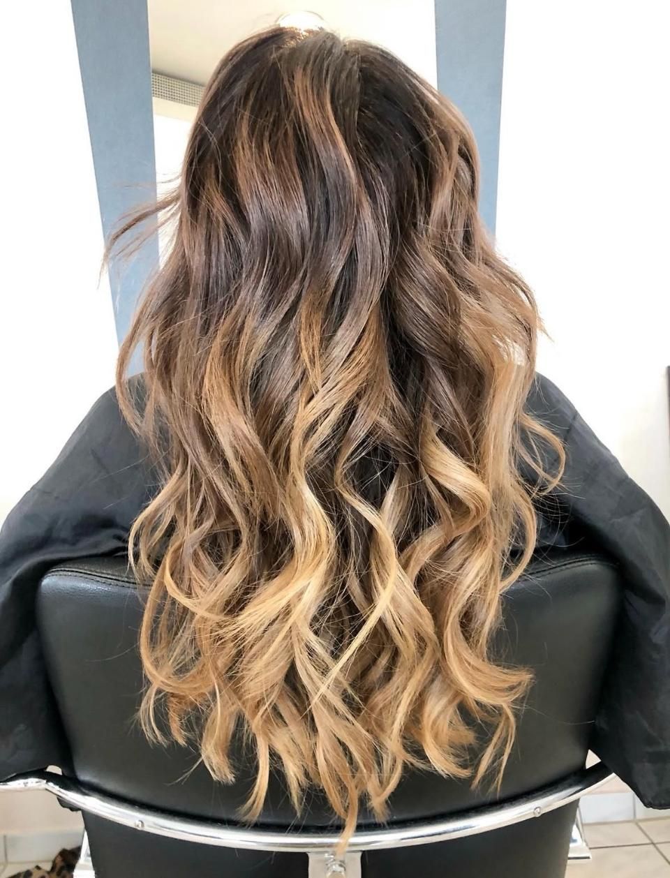 Langes, gewelltes, braun-blondes Ombré-Haar, von hinten gesehen, an einer Person, die in einem Friseurstuhl sitzt