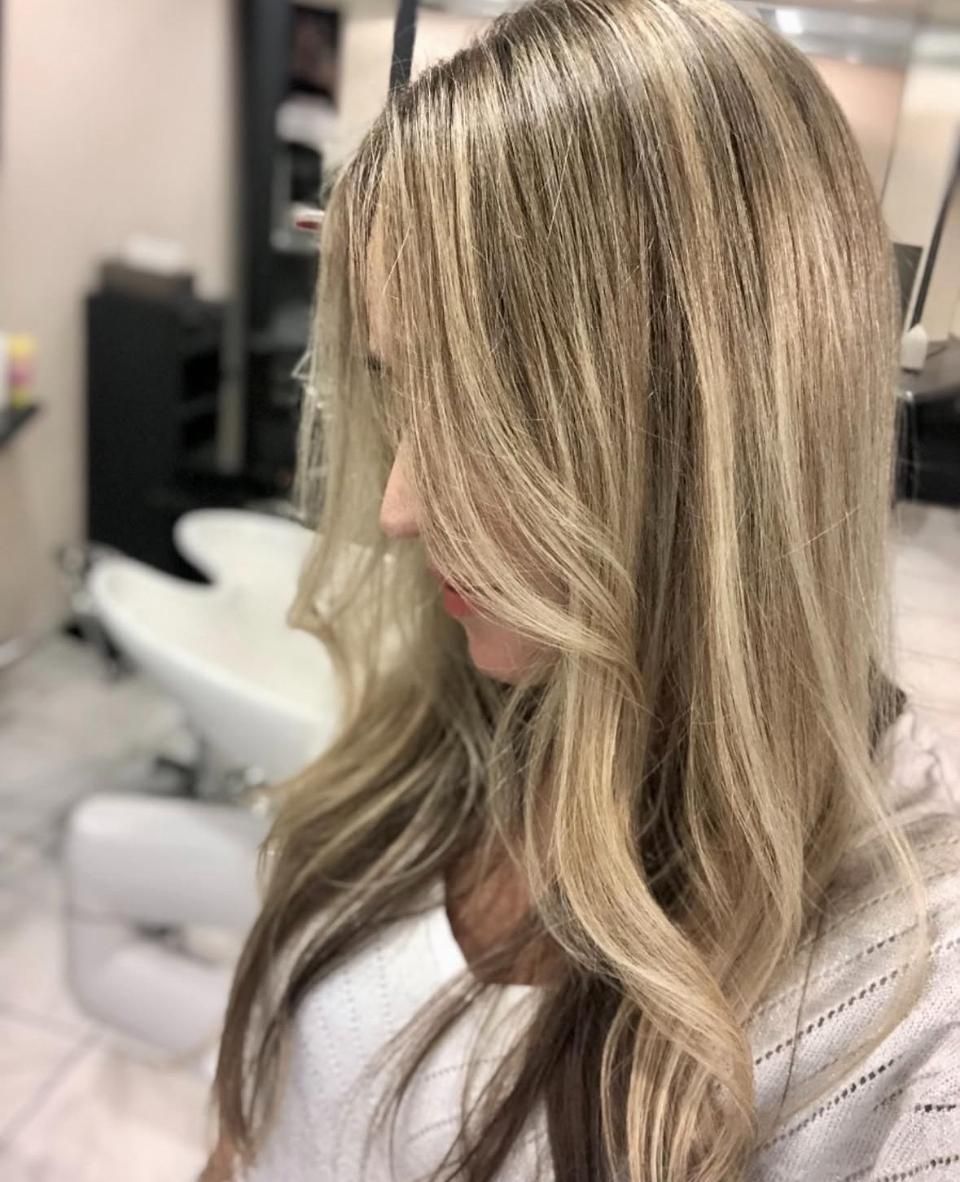 Frau mit langen blonden Haaren im Friseurstuhl, von der Seite vor hellem Salonhintergrund