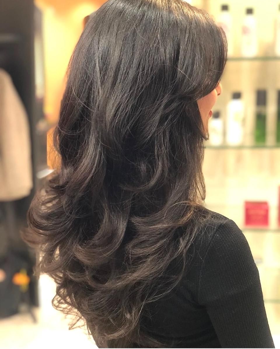 Seitenansicht einer Frau mit langem, gewelltem, dunklem Haar in einem Friseursalon.