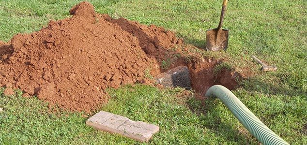 Un trou creusé dans l'herbe verte avec de la terre, un tuyau, une pelle et une brique.