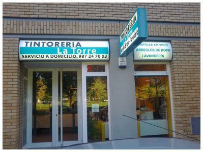 Fachada de una tintorería y lavandería con letreros azules y blancos en un edificio de ladrillo
