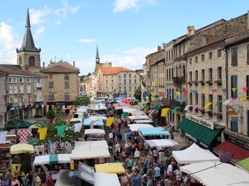 Marché en plein air bondé sur une rue historique européenne, avec des étals colorés et des clochers d'églises.
