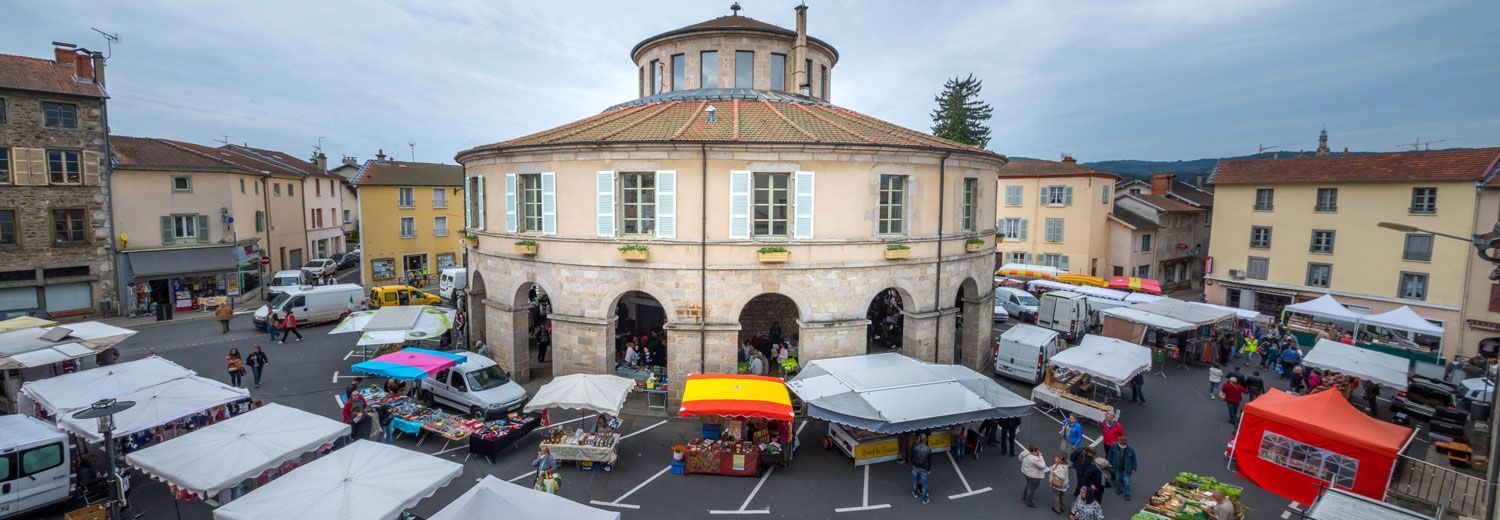 Place du village avec des étals de marché autour d'un bâtiment historique rond sous un ciel nuageux