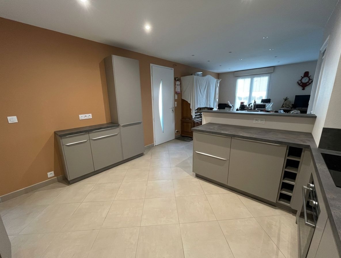Cuisine moderne avec un sol carrelé beige, un mur d’accent marron, des placards gris et un îlot près d’une fenêtre lumineuse