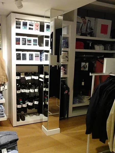 Magasin de vêtements avec des étagères garnies de vêtements pliés et des articles suspendus, ainsi qu’un présentoir miroir.
