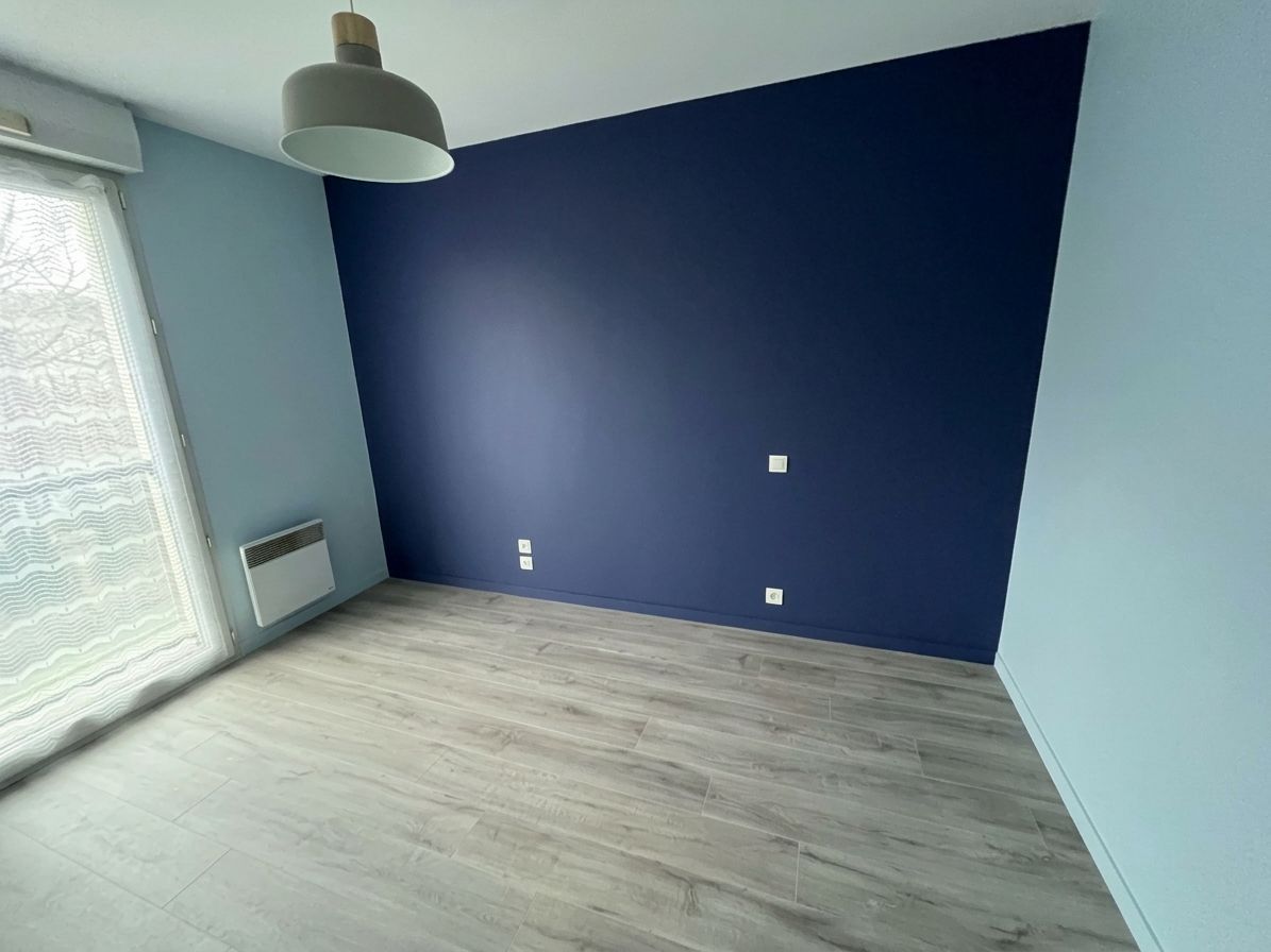 Pièce vide avec un mur d’accent bleu marine, un parquet clair, une fenêtre et un plafonnier.