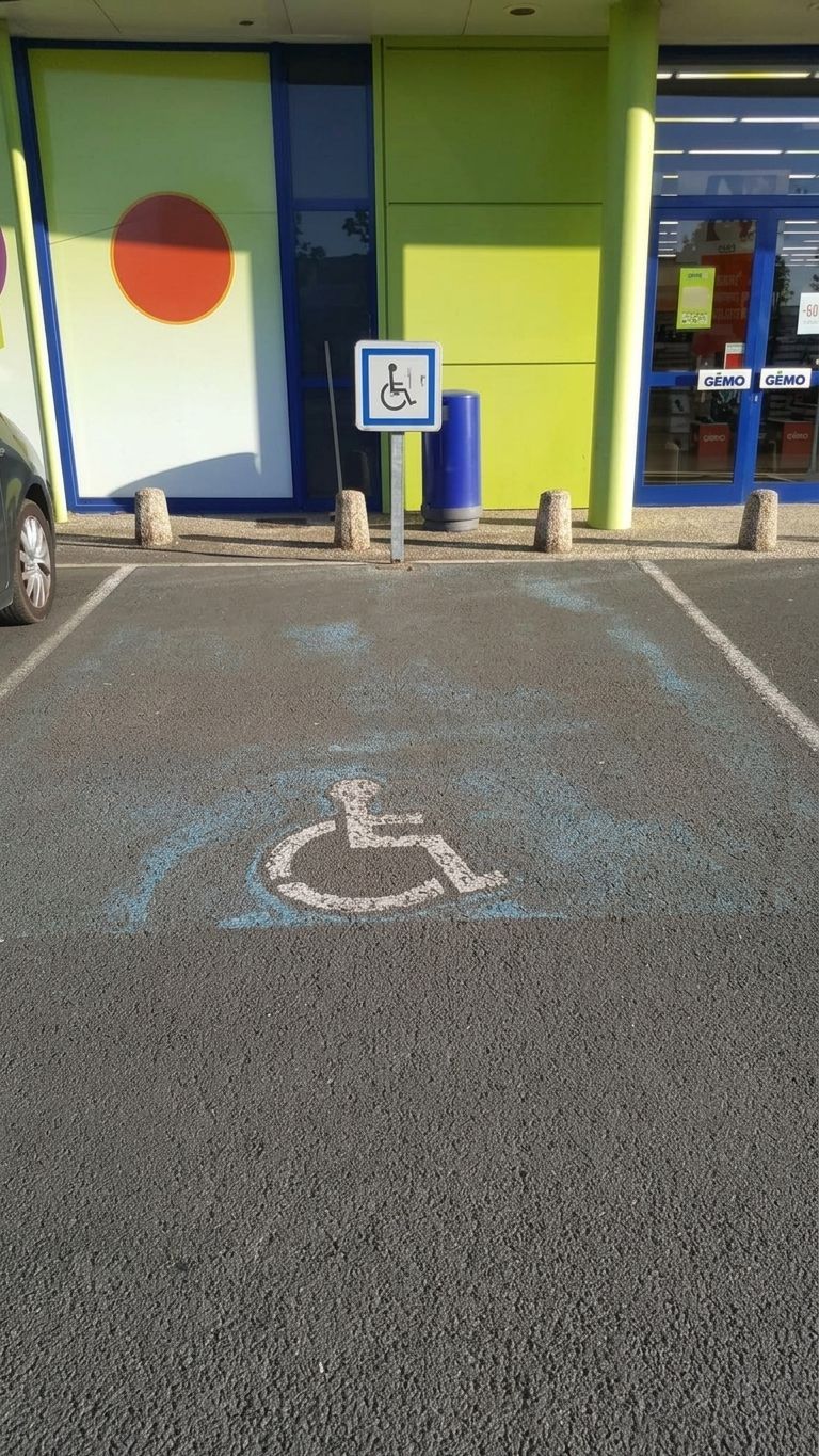 Place de stationnement accessible avec un symbole de fauteuil roulant, devant l’entrée d’un magasin.