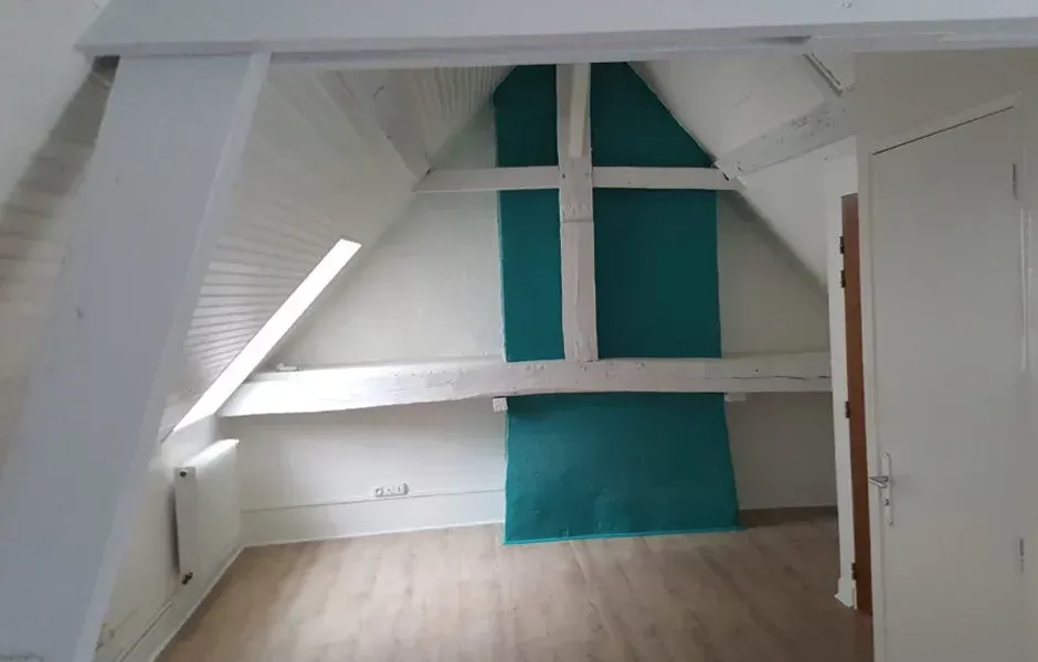 Chambre mansardée blanche avec poutres apparentes, panneaux muraux bleu sarcelle et parquet clair.