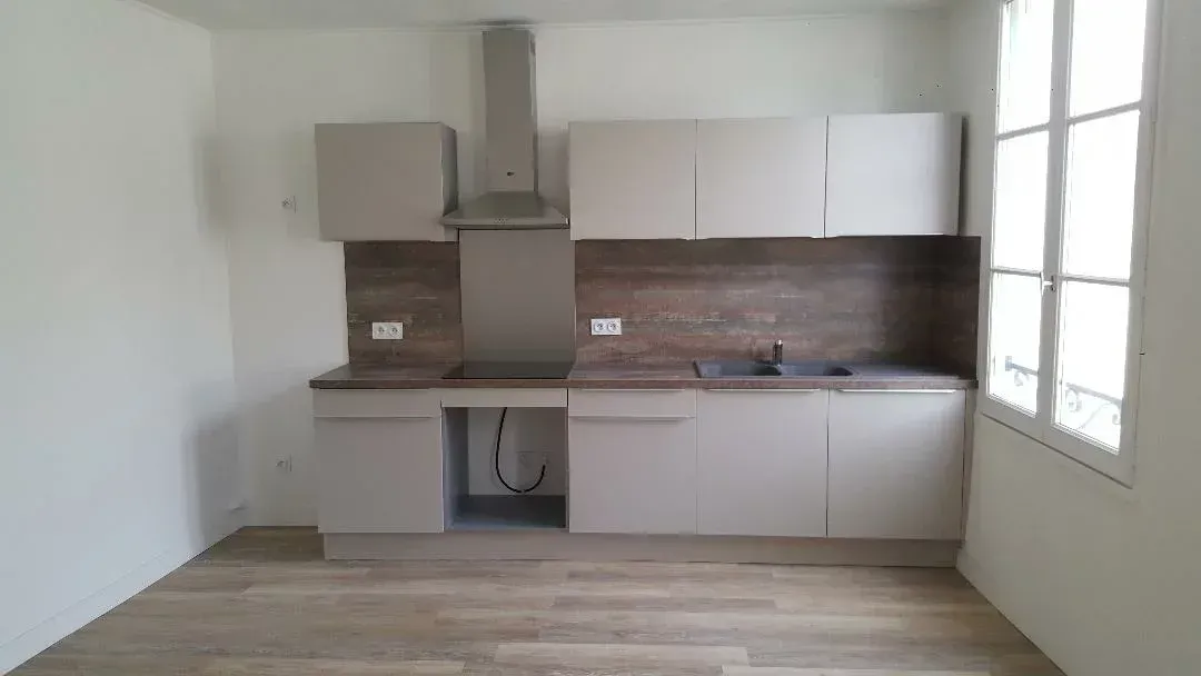 Cuisine vide avec des placards blancs, une crédence en bois et une grande fenêtre à droite