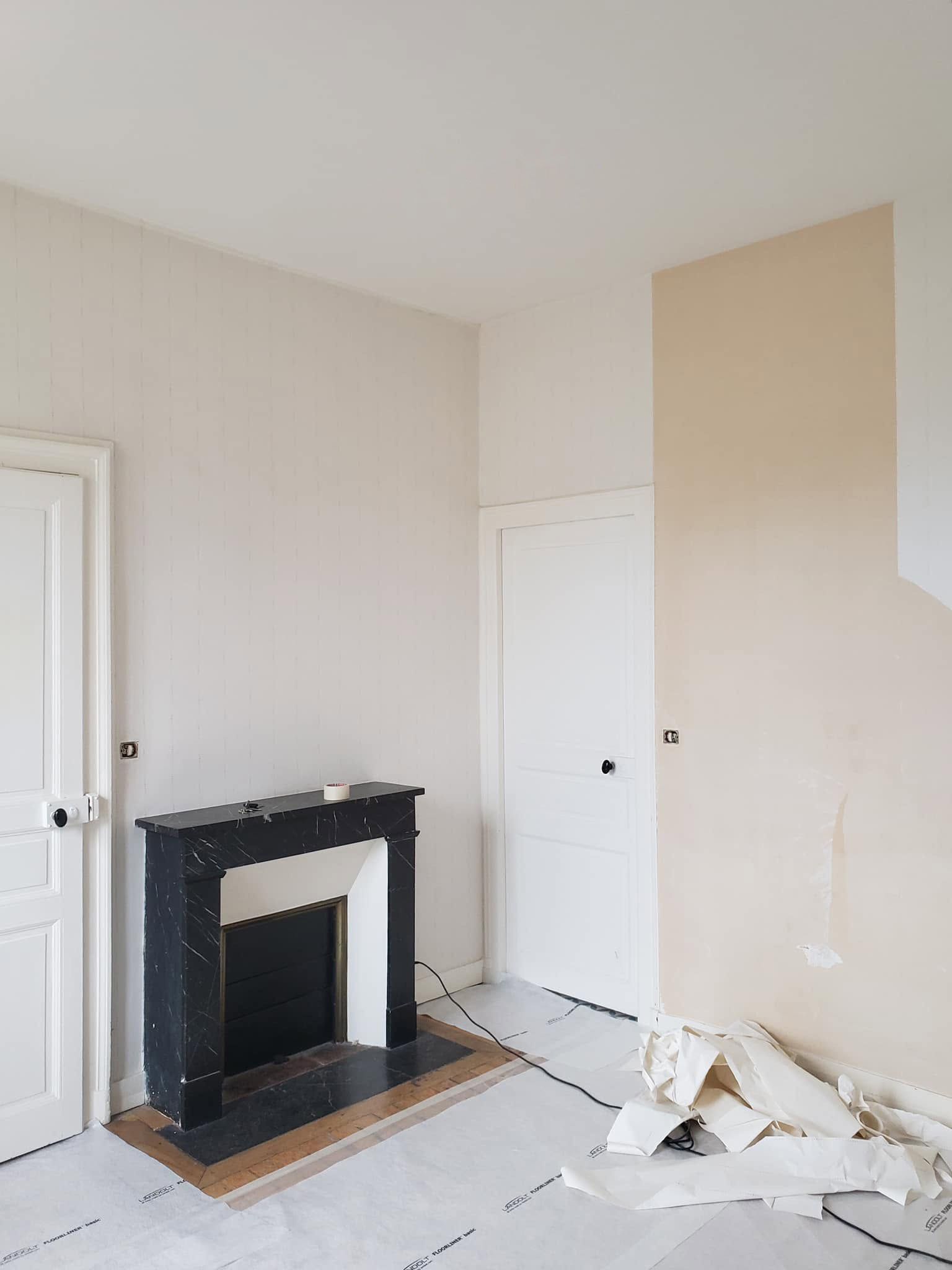 Pièce en cours de rénovation, avec une cheminée noire inachevée, des portes blanches et des débris de plâtre au sol