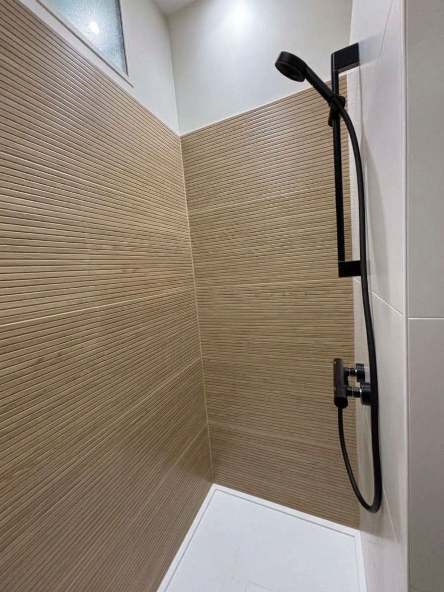 Cabine de douche compacte avec des parois beiges texturées et une douchette noire