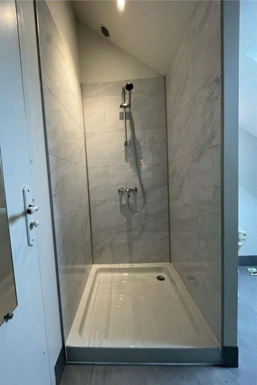 Petite cabine de douche carrelée avec douchette à main et receveur blanc