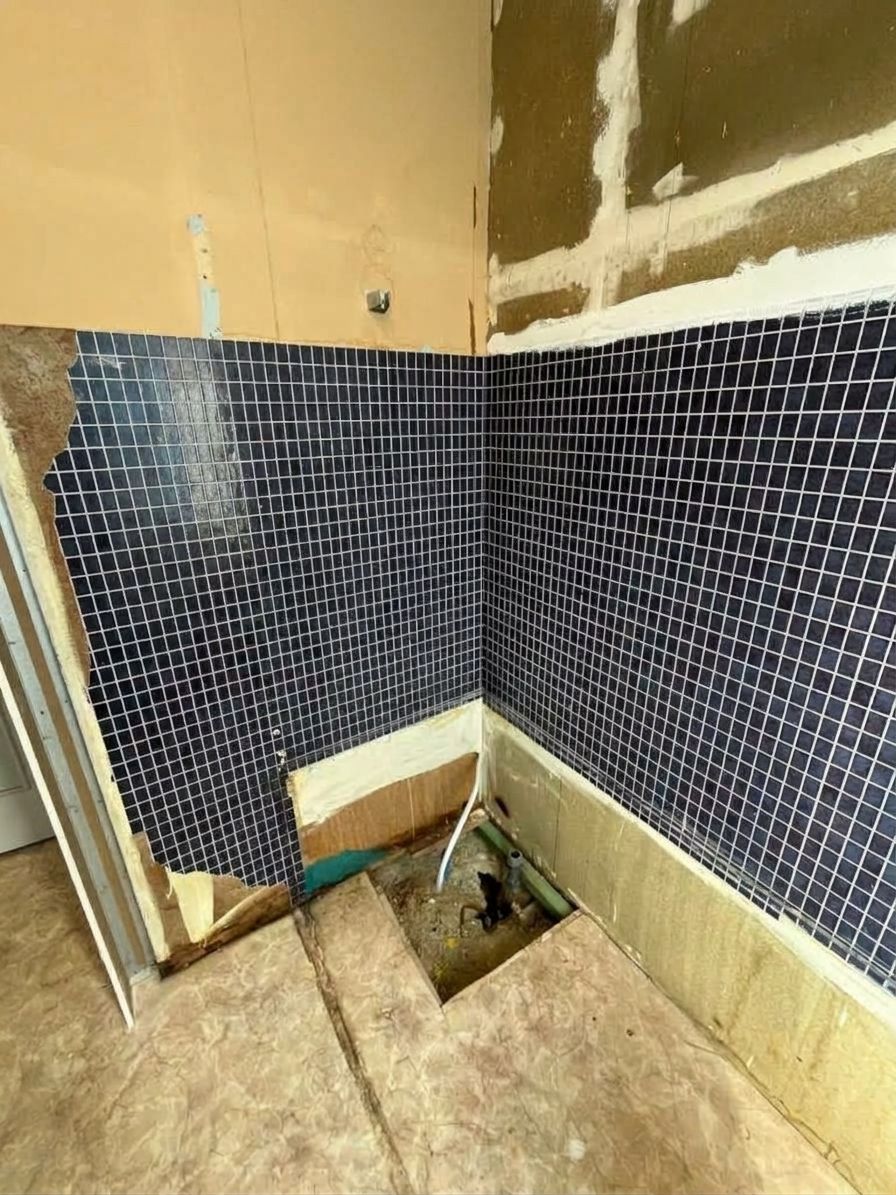 Angle d’un mur de salle de bains partiellement carrelé, avec la plomberie apparente et le sol encore en travaux