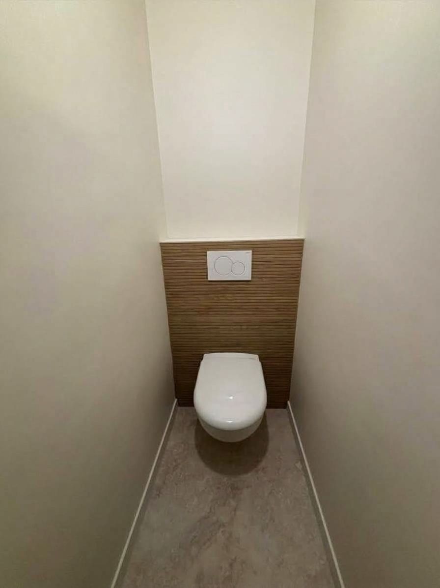 Petite salle de bains avec des boiseries derrière un WC suspendu